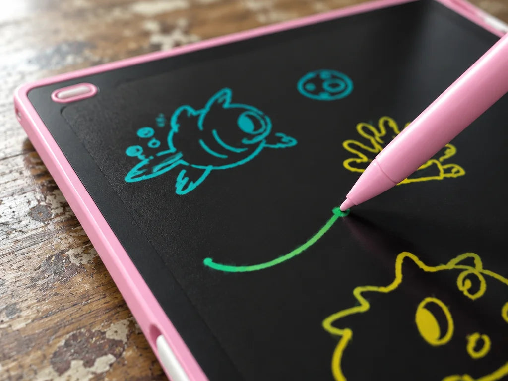 A close usage photograph of the exact pink LCD tablet from the reference on a worn kitchen table. Th